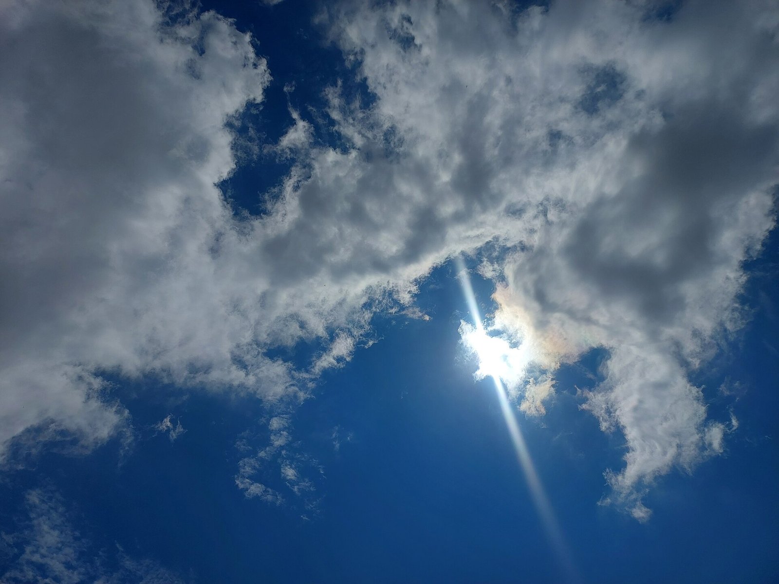 The sun blazing through clouds in a blue sky