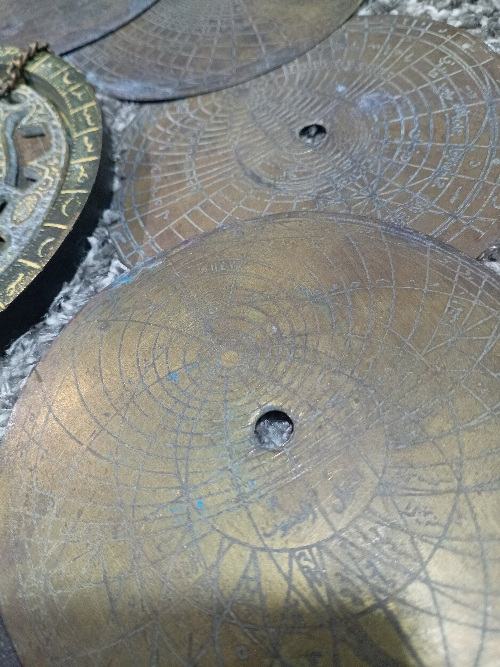 A close-up of worn brass astrolabe plates covered in fine engraved coordinate grids.