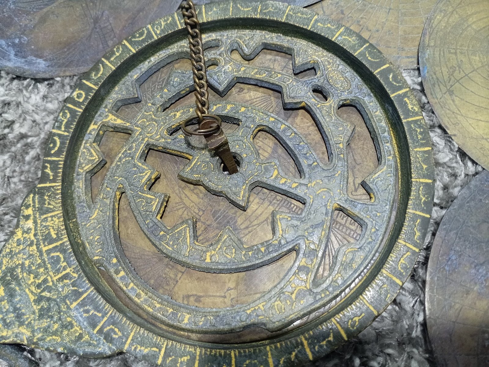 The back of an old brass astrolabe with its pierced star map and hanging chain.