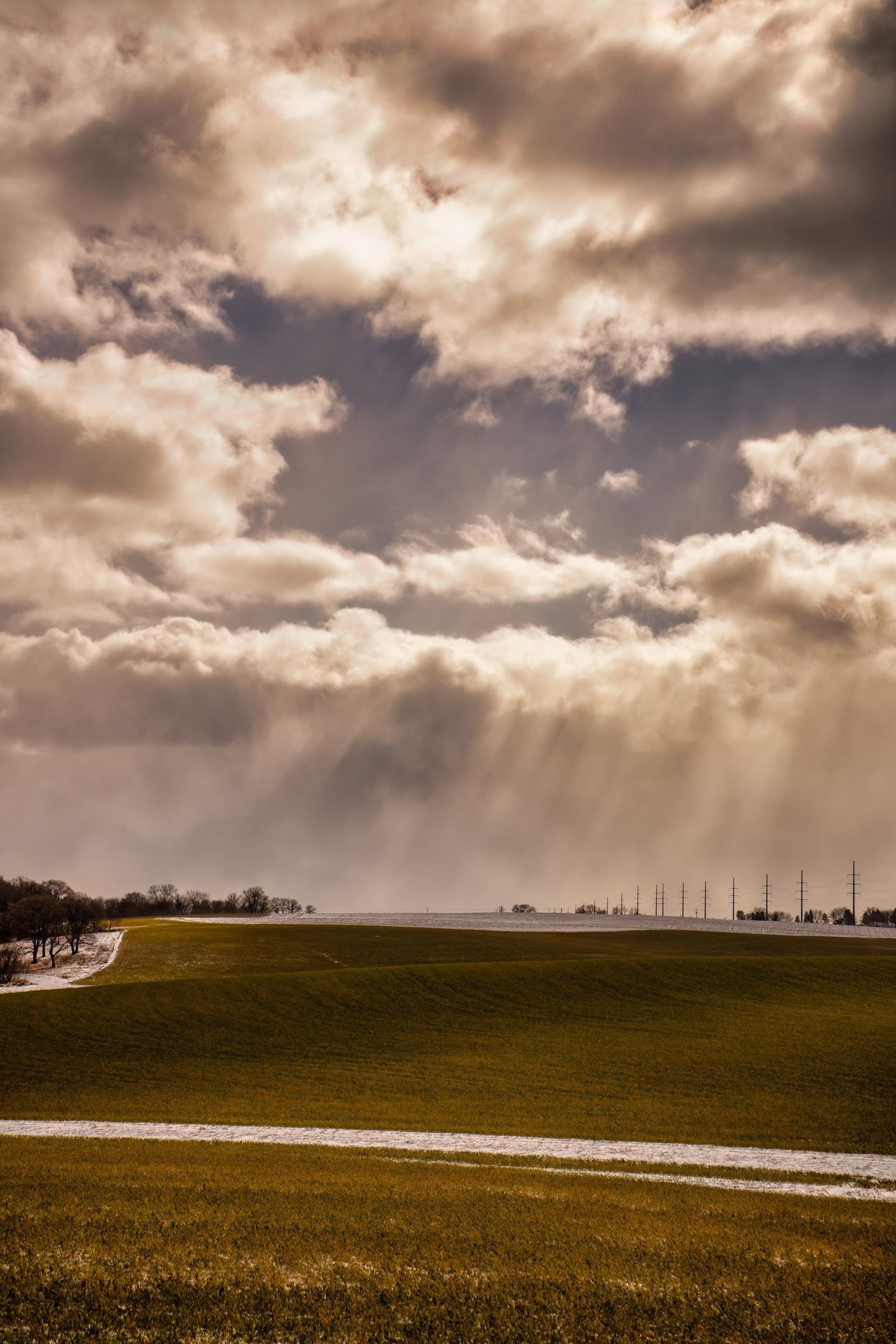 Dark storm clouds breaking apart over a green field, pale sunlight appearing along the horizon.