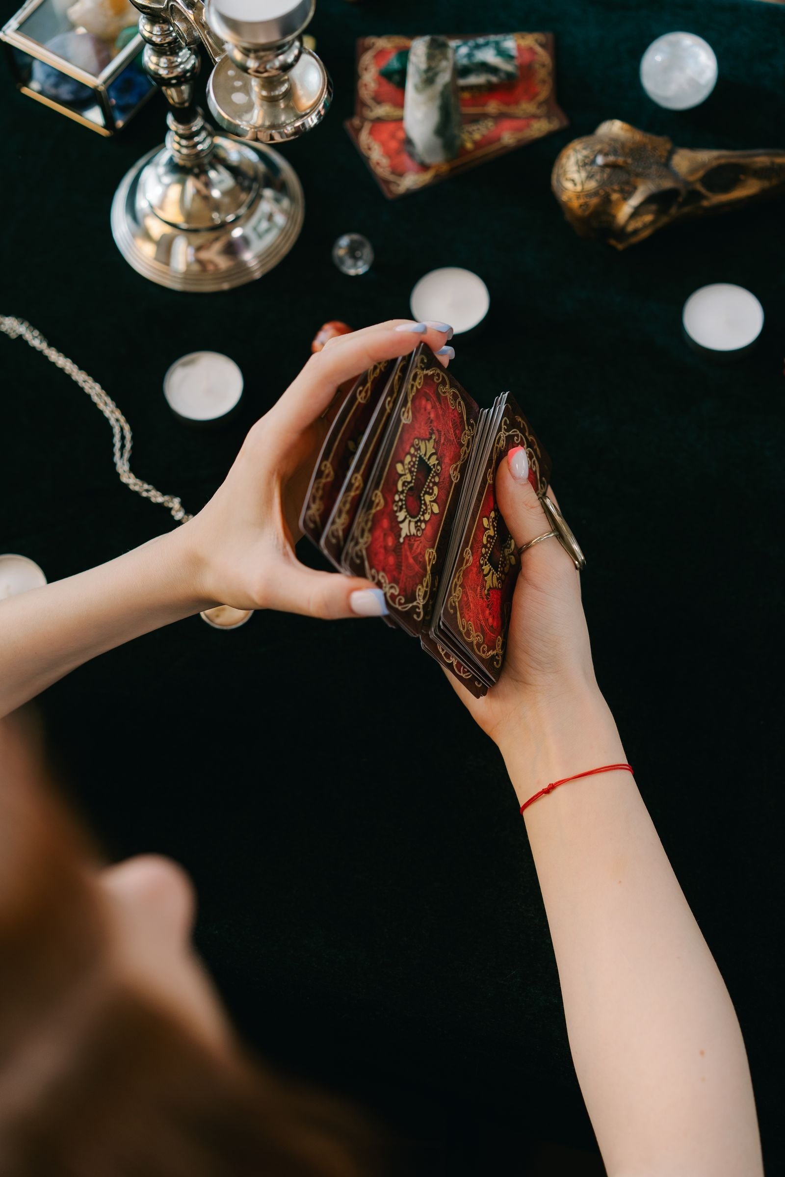 Two hands shuffling a tarot deck with red and gold card backs on a dark green table.