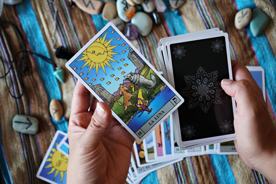 Hands holding the Sun tarot card and a smartphone, a modern tarot app in use.