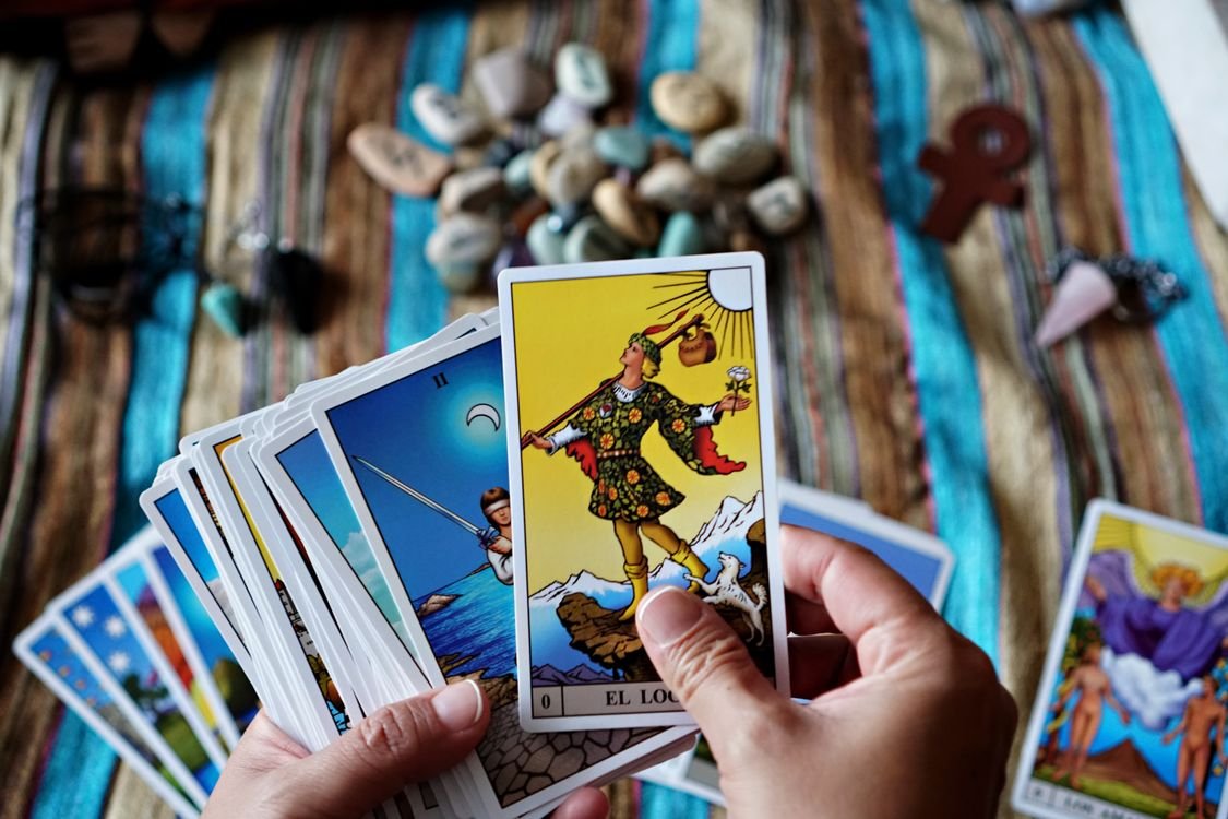 Hands holding the Devil tarot card above a fanned deck.
