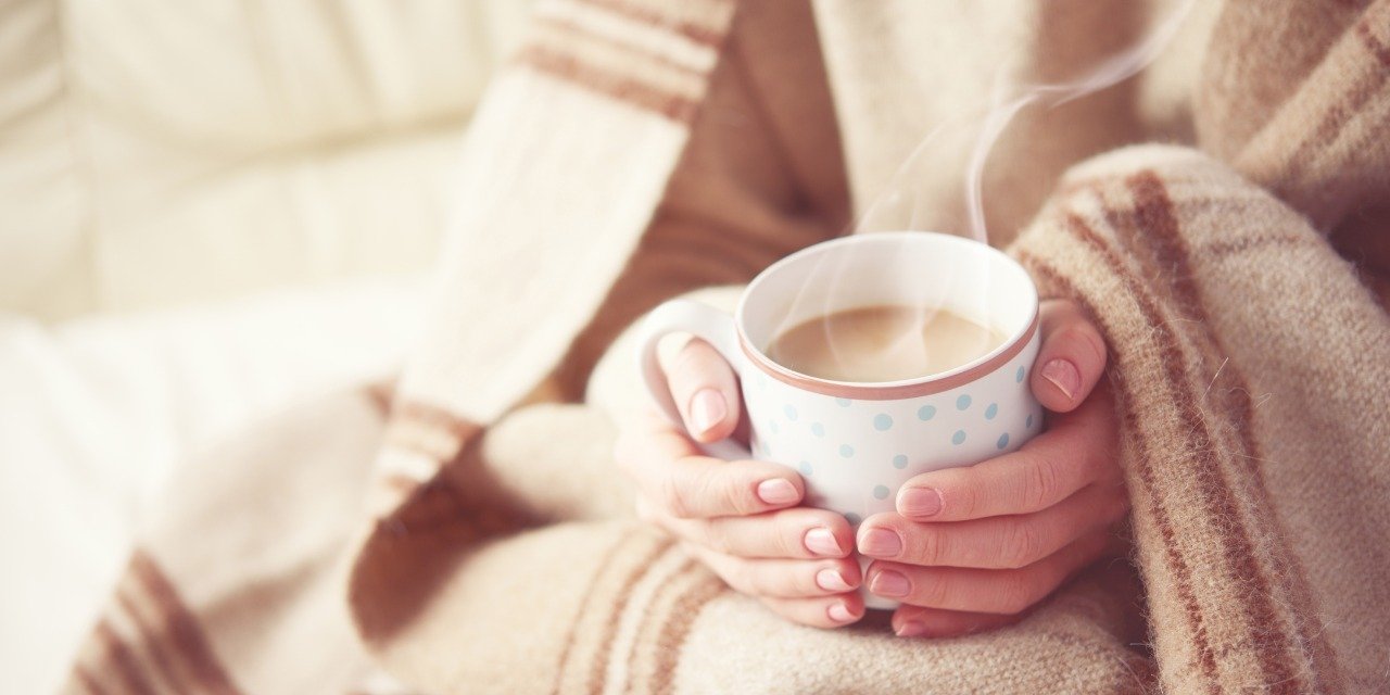 A person wrapped in a knitted blanket holding a warm mug