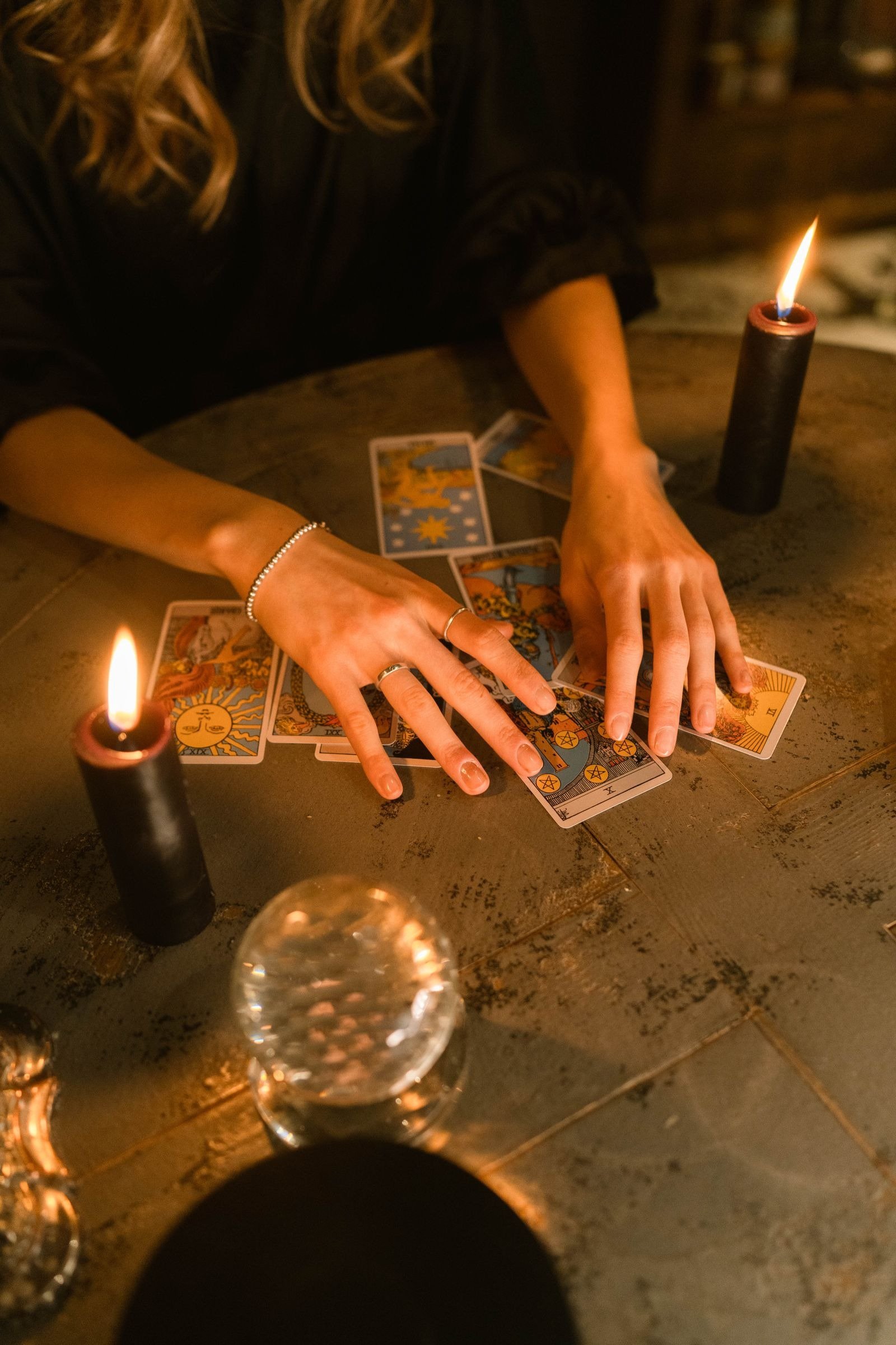 Hands arranging Rider-Waite tarot cards on a wooden table lit by candles.