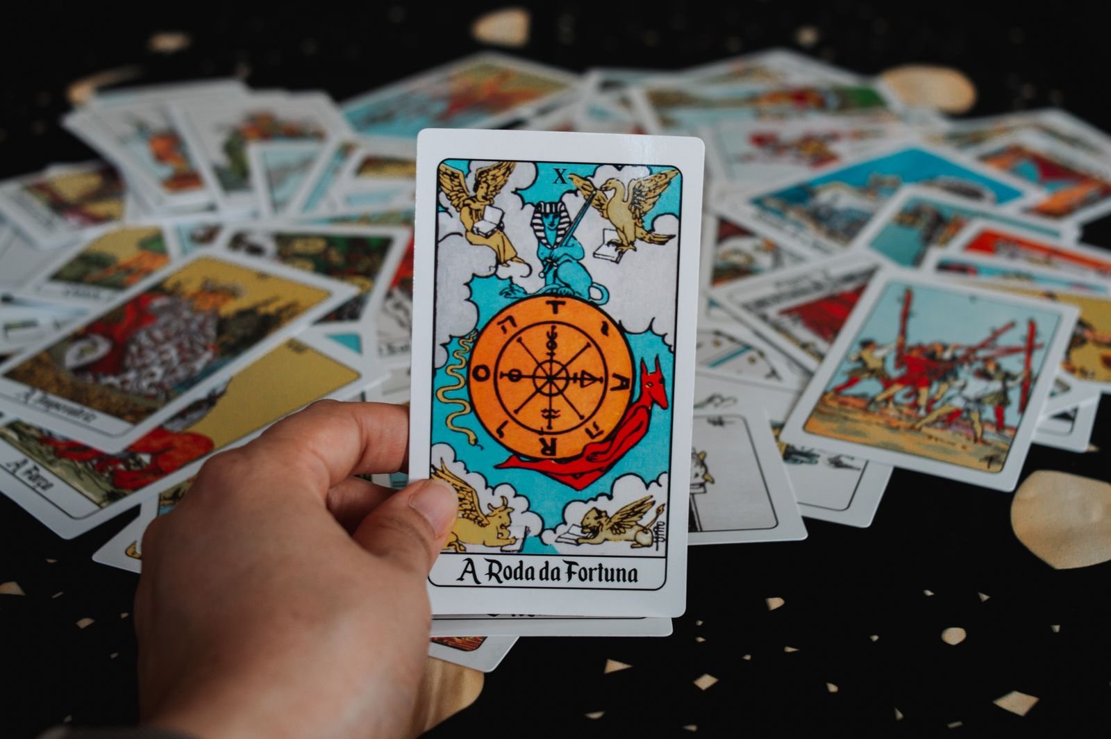 A hand holding the Wheel of Fortune tarot card over scattered cards