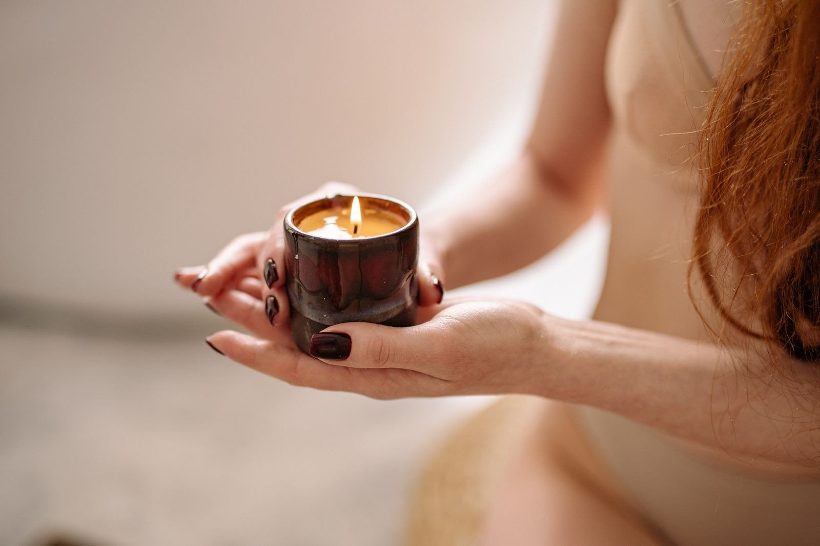 A woman holding a lit candle in a ceramic holder with both hands.
