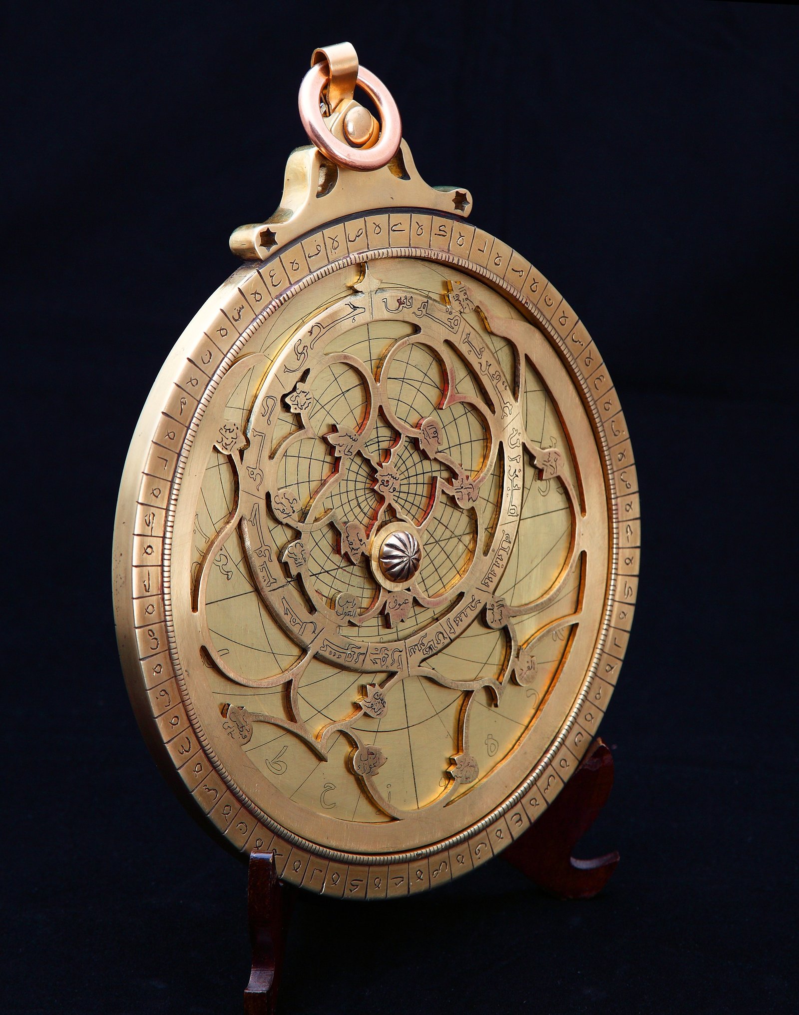 A brass Iranian astrolabe with engraved markings, displayed on a stand.