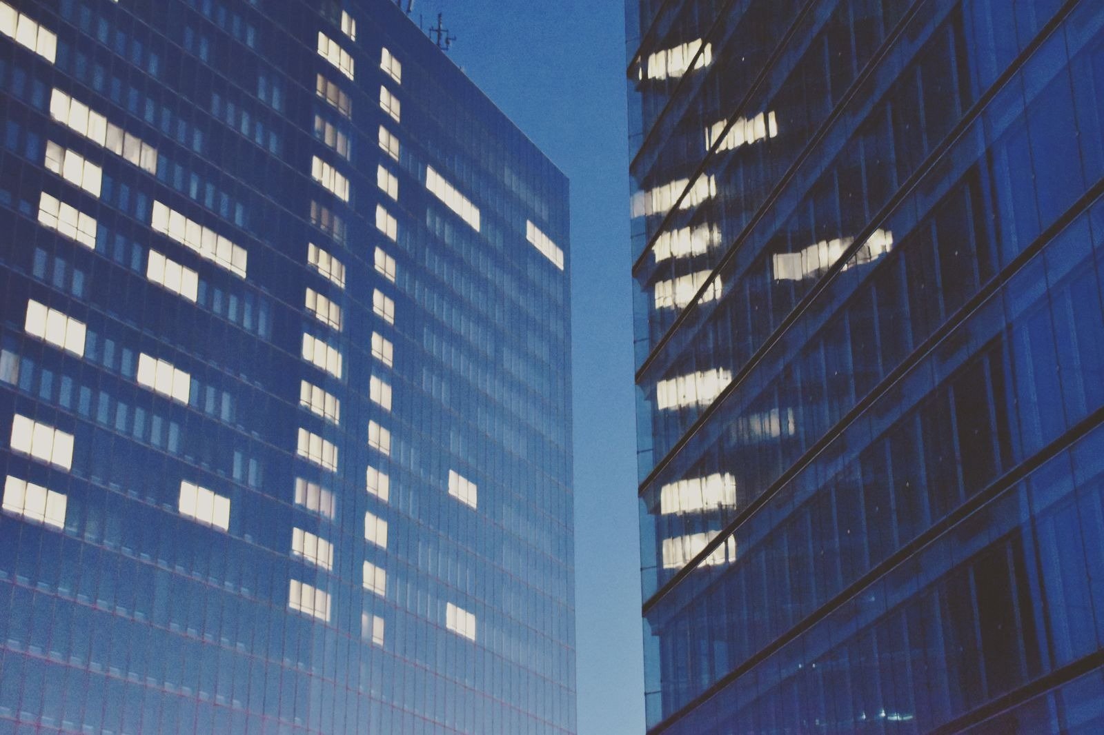 Two glass office towers with lit windows against a deep blue twilight sky.