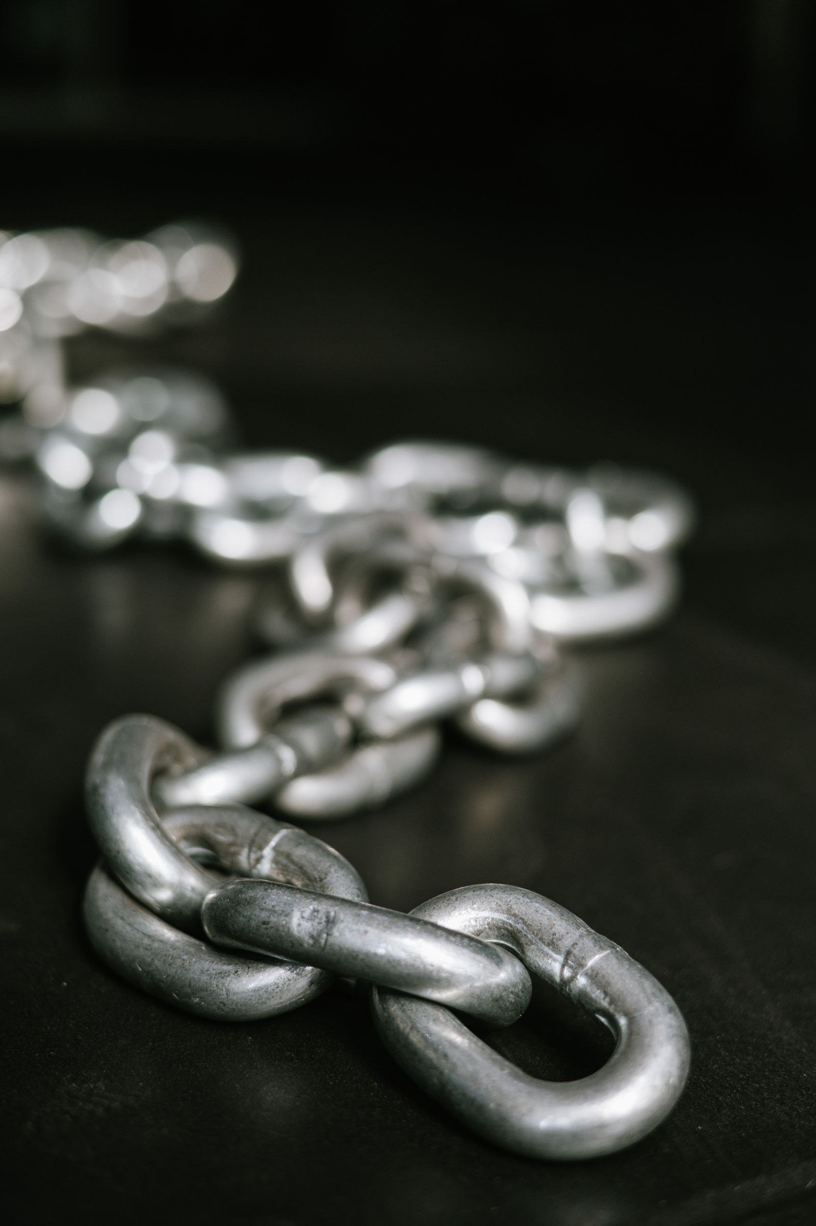 A heavy iron chain coiled on dark wood, one link visibly broken open.