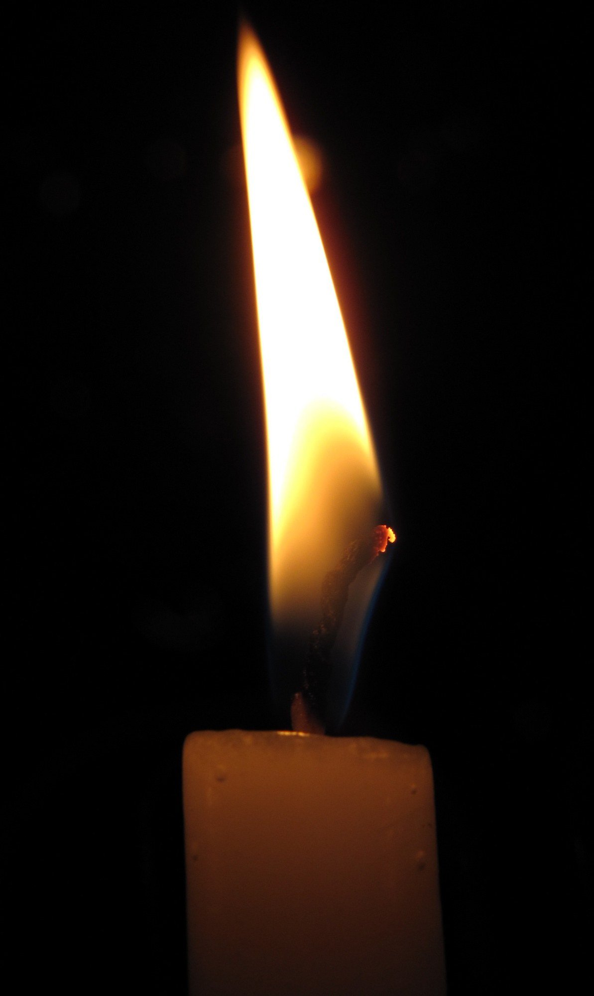 A single candle flame burning in a dark room, wax pooled around its base.