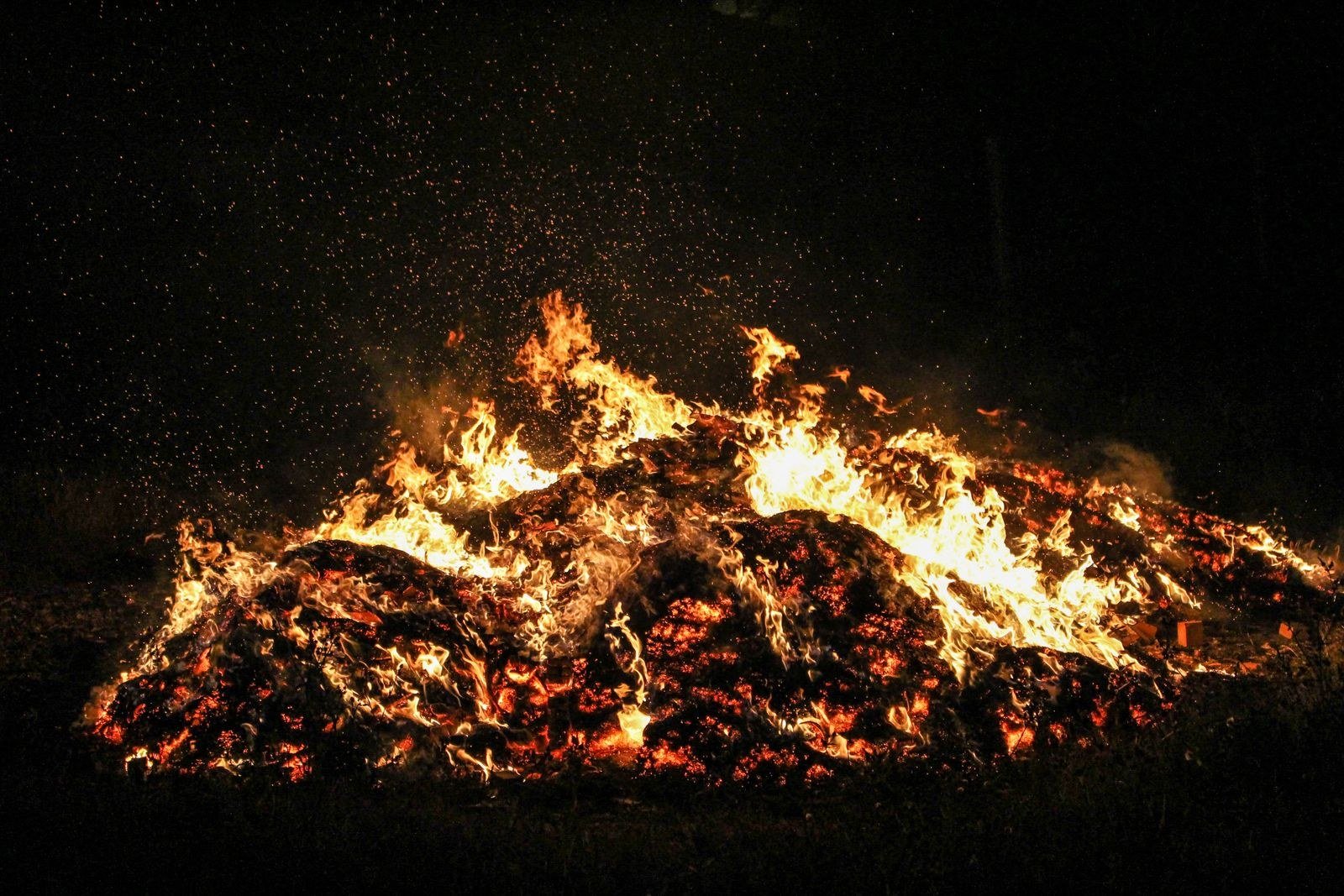 Large bonfire with flames and sparks rising into the night sky.