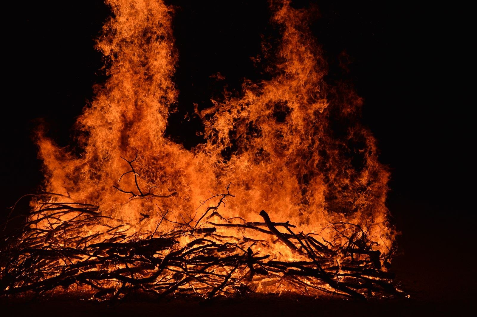 Tall orange flames rising from a bonfire of branches against the night sky.