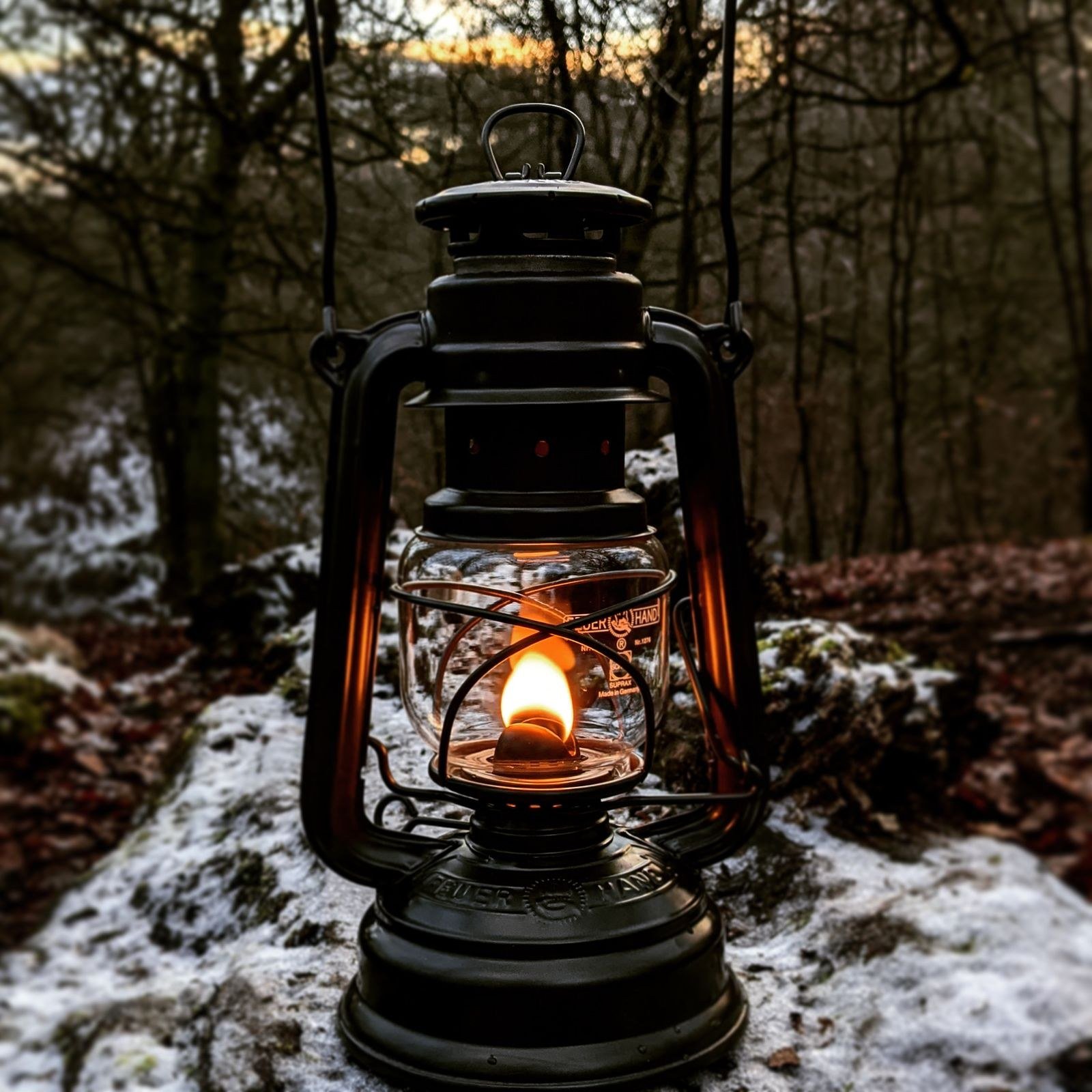 A single lantern glowing warm on a wooden table in a dark room.