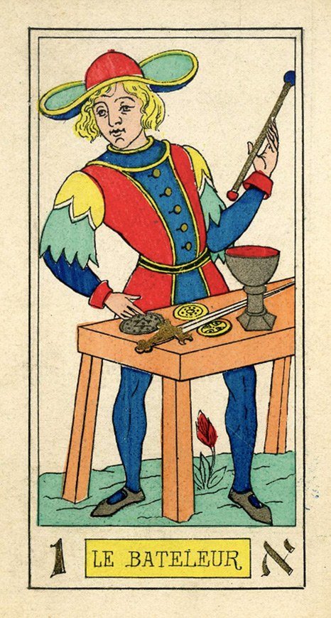 The Bateleur card from Oswald Wirth's 1889 tarot deck, showing a young man in a wide red-and-green hat and colorful tunic holding a wand, behind a table with a chalice, coins, and a sword.