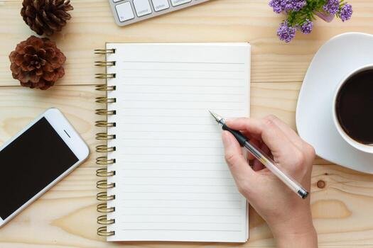 A hand writing in a notebook on a wooden desk