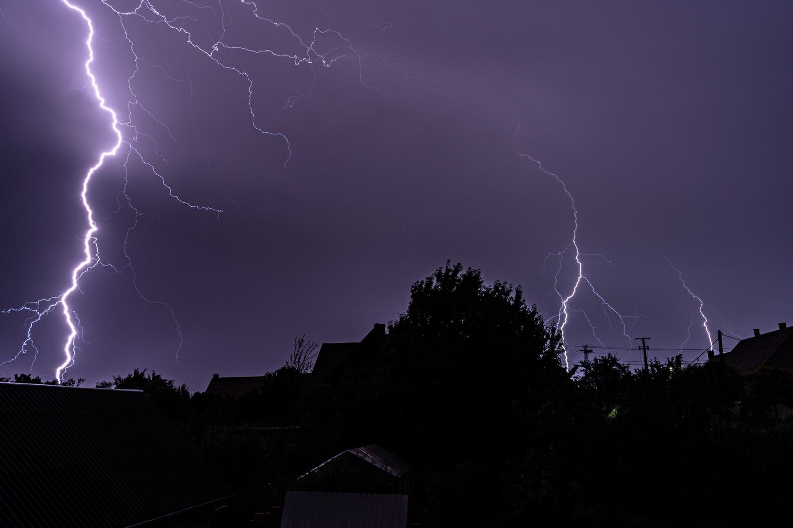 A fork of lightning striking through dark storm clouds over a distant landscape.