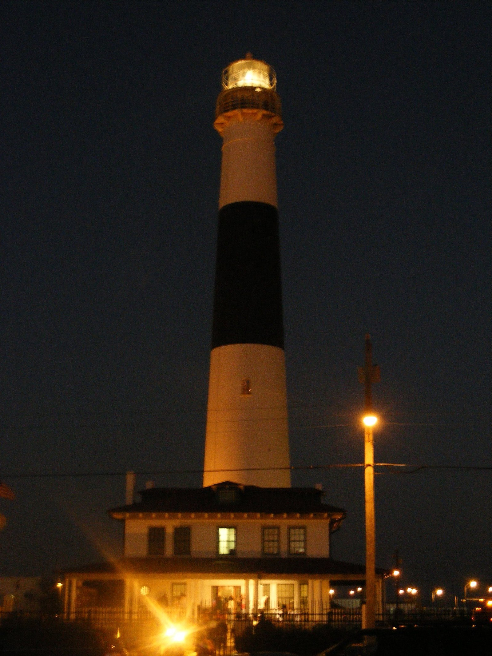 Absecon Lighthouse lit up at night, its black and white tower glowing above a lit keeper's house