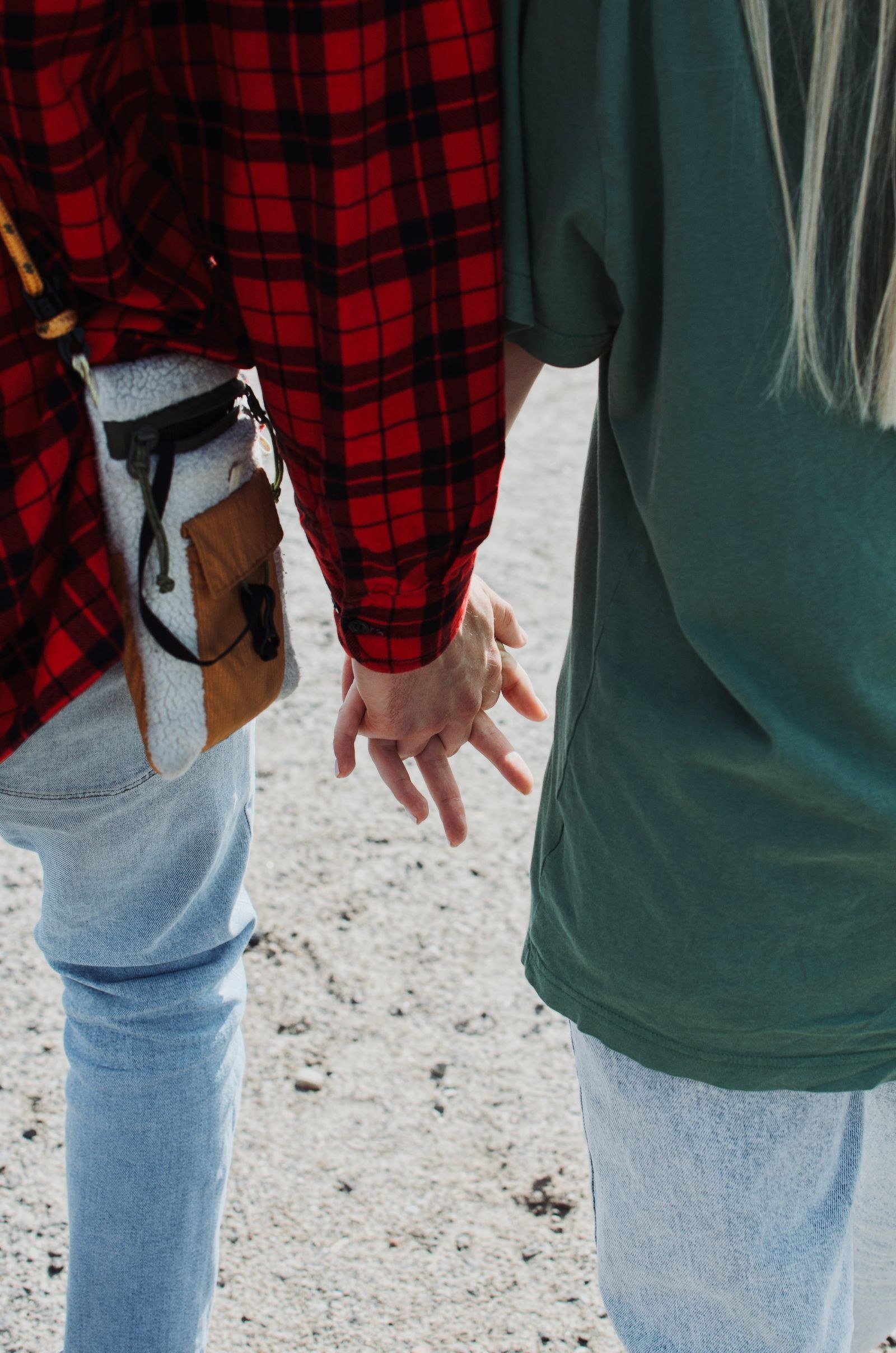 Close-up of a couple holding hands while walking, one wearing a red plaid shirt.