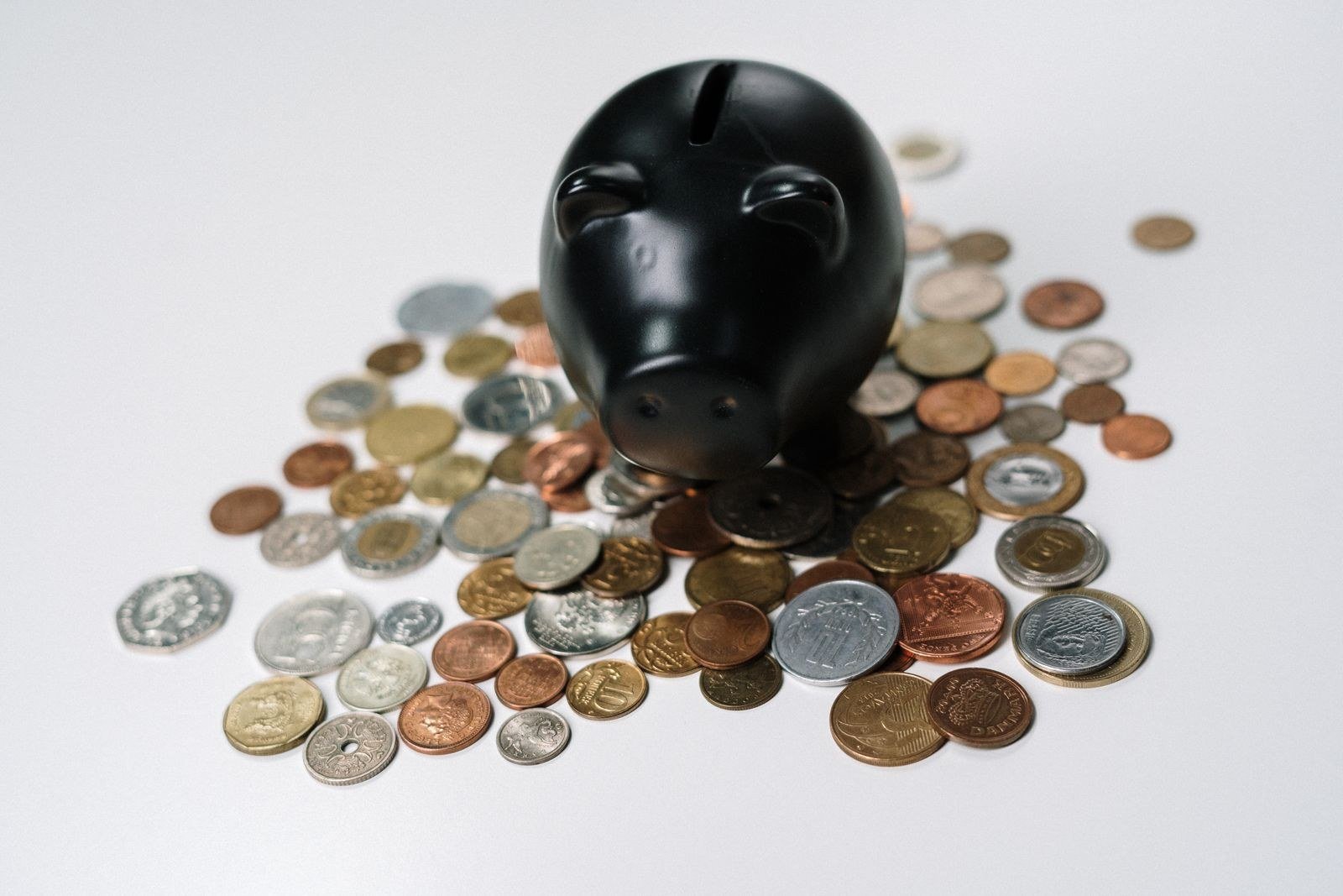 A black piggy bank surrounded by scattered coins on a white surface.
