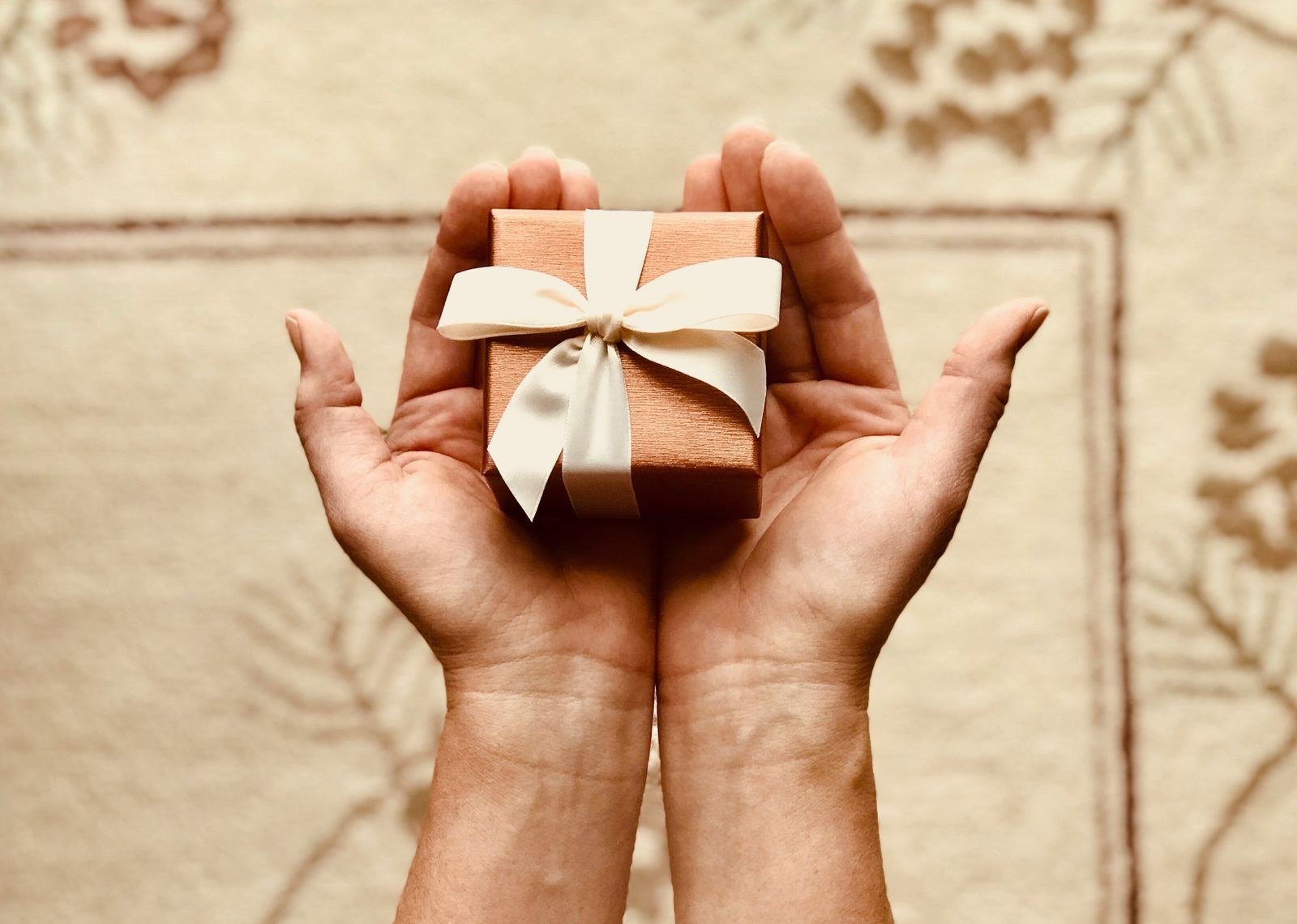 Two hands holding a small gift box tied with a white ribbon.