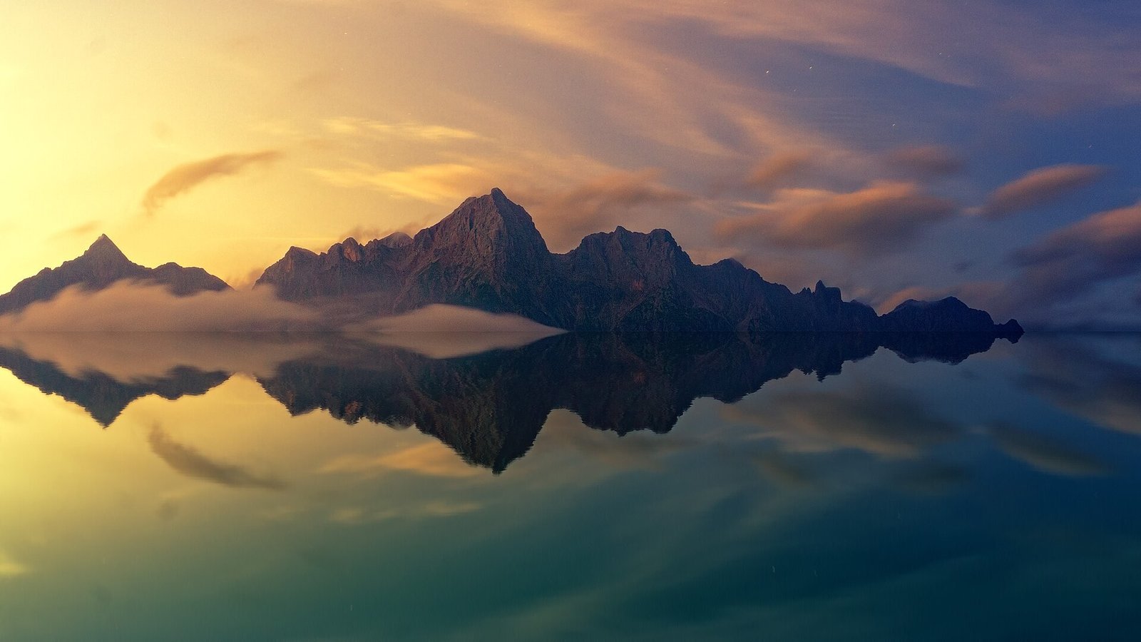 A calm mountain lake at dawn perfectly mirroring the peaks and pink sky above, mist hovering over the still water.