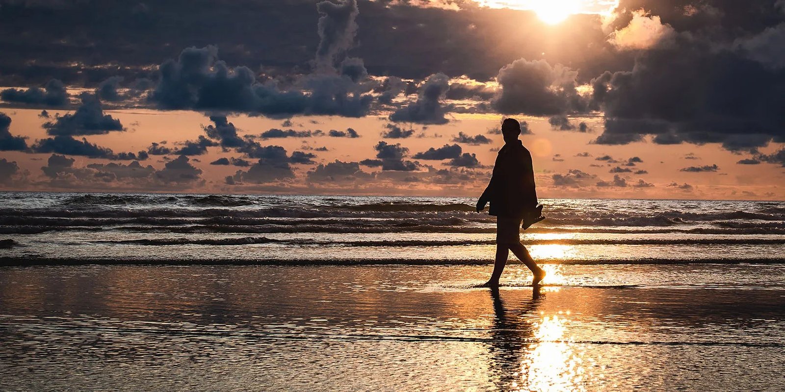 A person walking alone on a beach at sunset