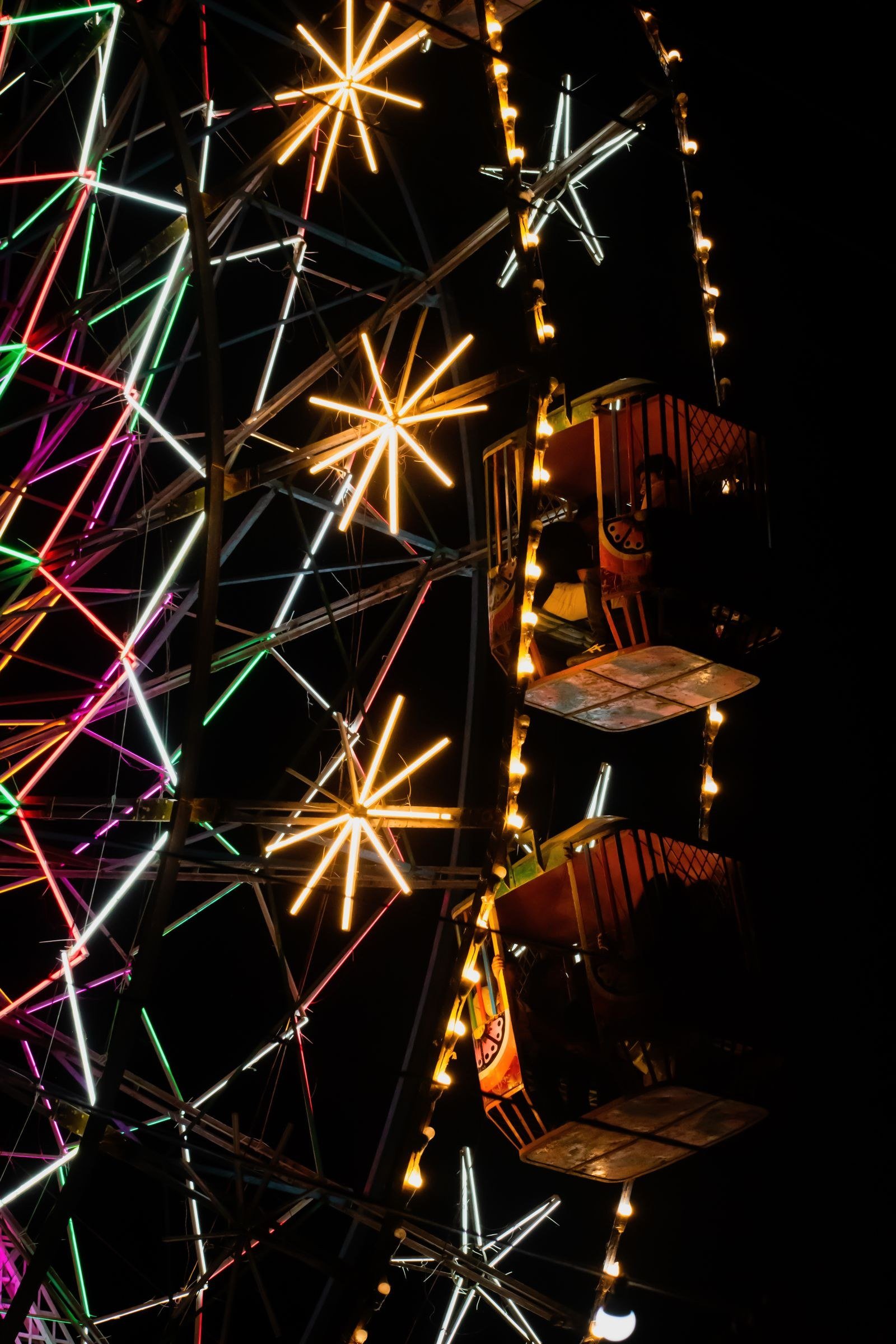 Ferris wheel with colorful neon lights and starburst decorations at night.