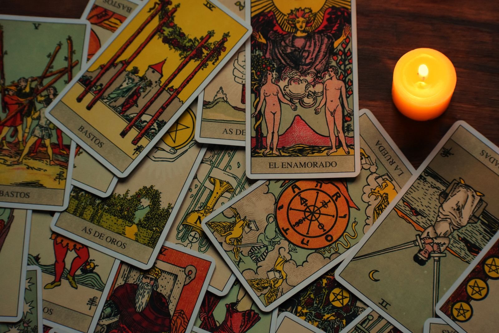 Tarot cards scattered on a wooden table beside a lit candle